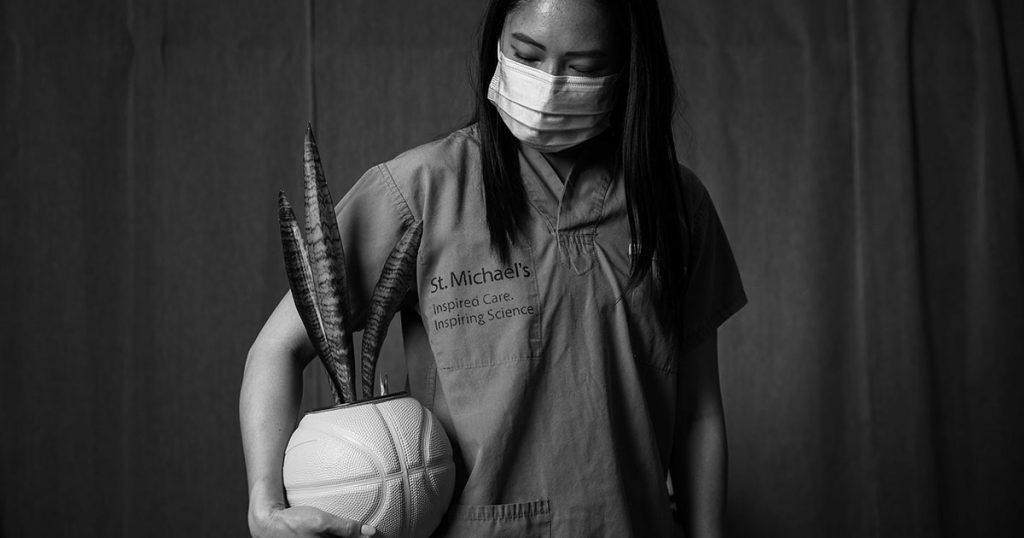 Olivia Ho, wearing scrubs and a face mask, holds onto a basketball planter she created.