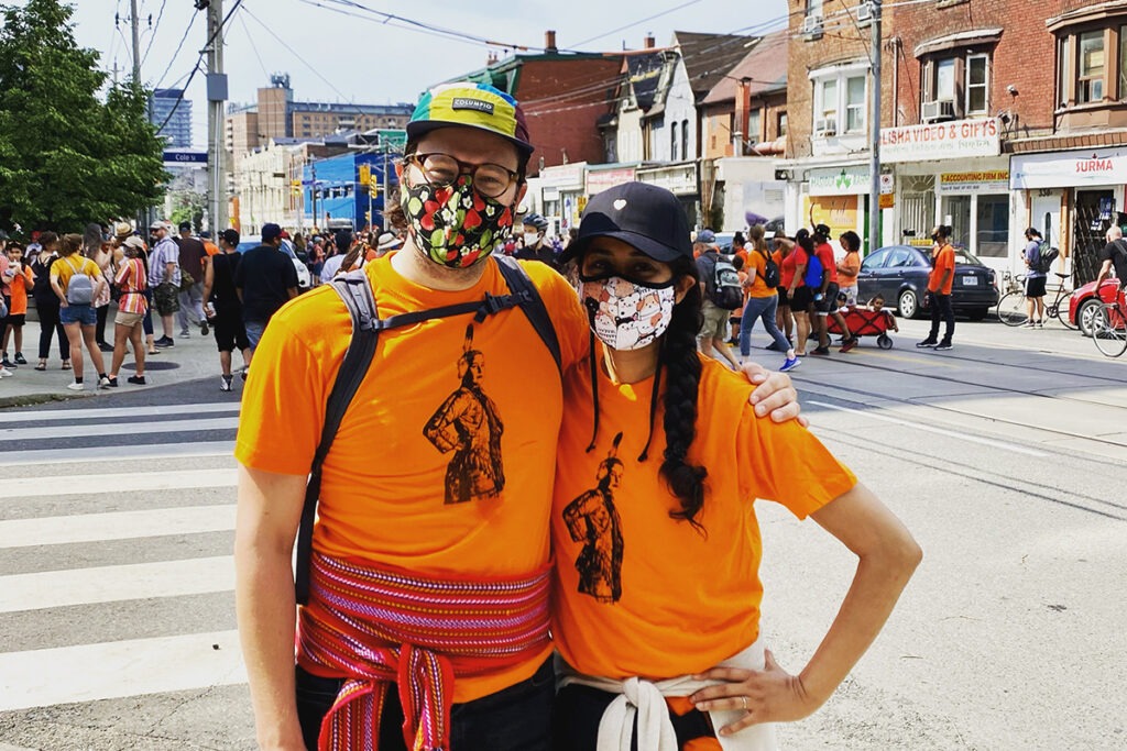 Dr. Giroux and Dr. Suleman stand at a street corner, wearing orange shirts, at an Every Child Matters March.