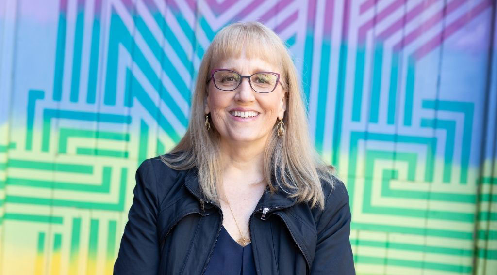 Dr. Sharon Straus stands in front of a multicolour background.