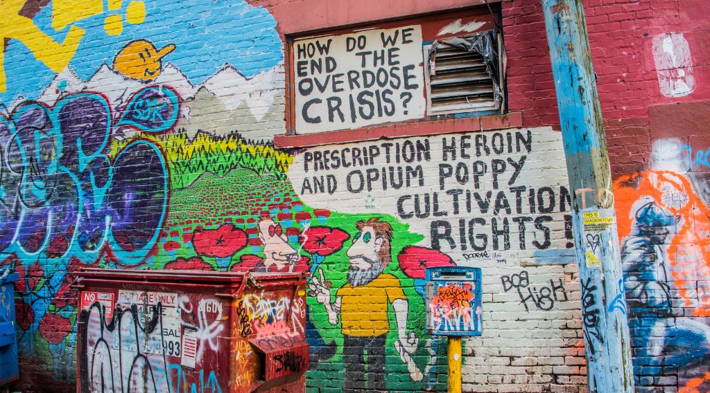 Graffiti art on a building wall in Vancouver. Caption reads, "How do we end the opioid crisis? Prescription heroin and opium poppy cultivation rights!"