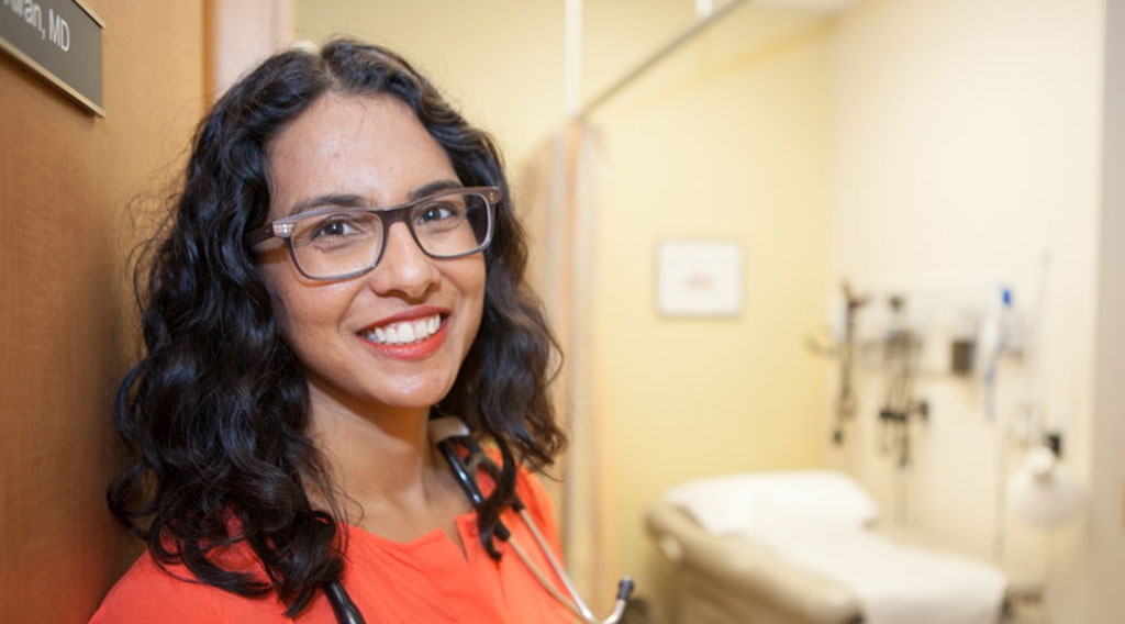 Dr. Tara Kiran stands at the doorway to her office with medical equipment in a soft focus in the background.