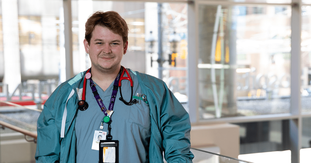 Conor Goulden, wearing hospital scrubs, stands in the lobby of the Peter Gilgan Patient Care Tower at St. Michael's Hospital.