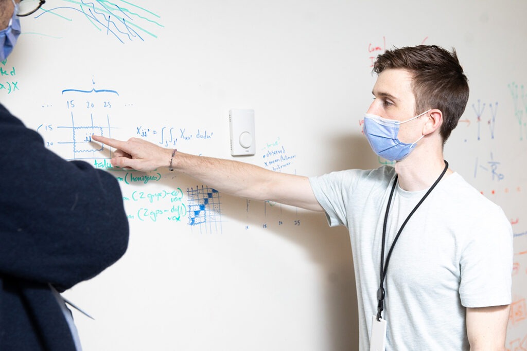 Jesse Knight points to a formula written on a whiteboard while a colleague looks on.