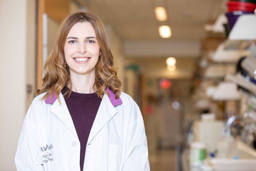 Dr. Veronique Miron, wearing a lab coat, stands in a hosptial hallway.