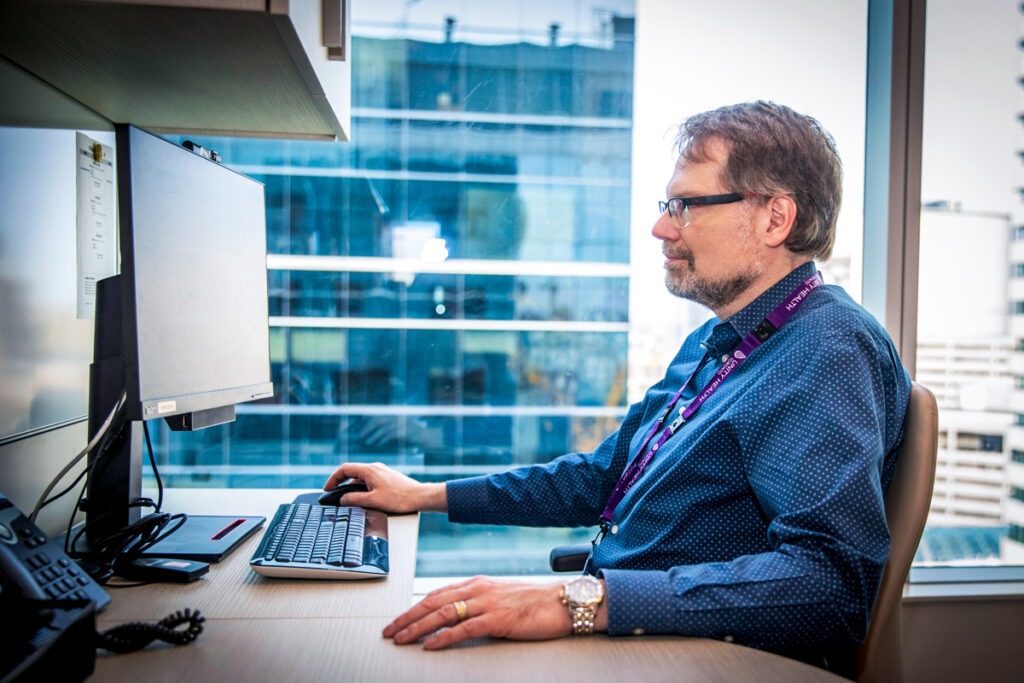 Dr. James Marriott sits at a desk and studies a MuScRAT report on a computer monitor.